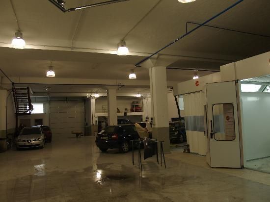 Un coche está aparcado en un garaje junto a una cabina de pintura.