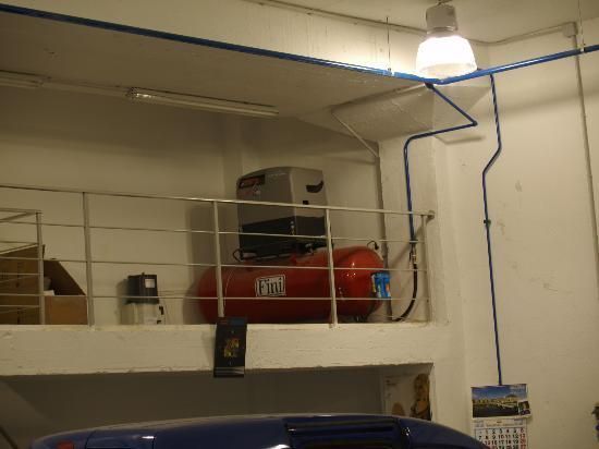 Un coche azul está aparcado en un garaje junto a un compresor de aire rojo.
