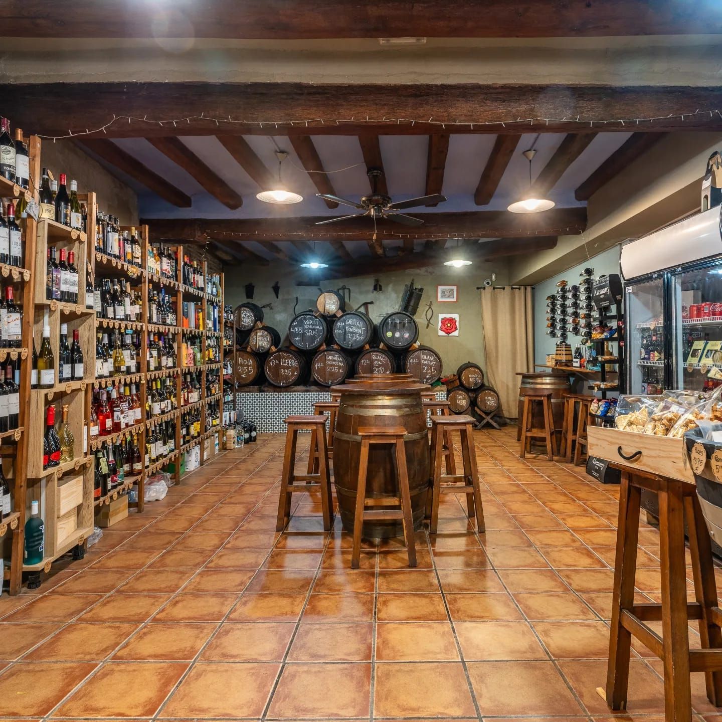 Una vinoteca con estanterías de madera repletas de botellas, una mesa central hecha con un barril y taburetes