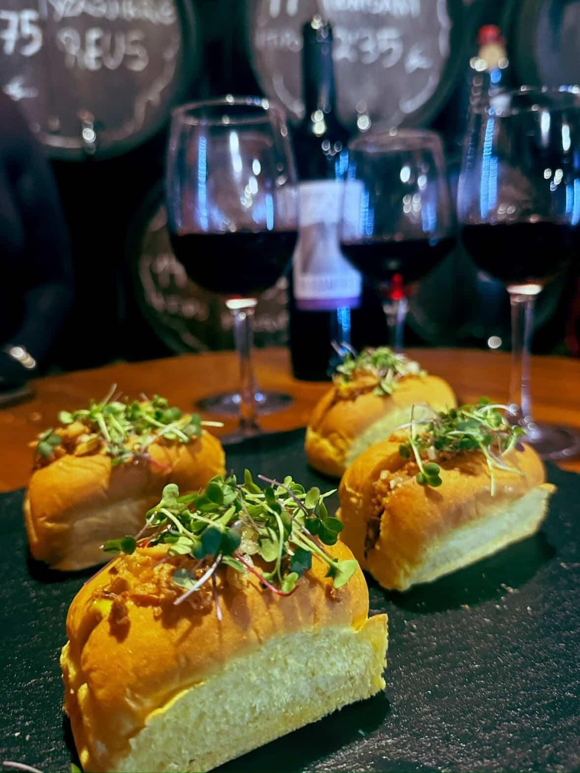 Tres mini hamburguesas cubiertas con microvegetales reposan sobre una tabla de pizarra oscura