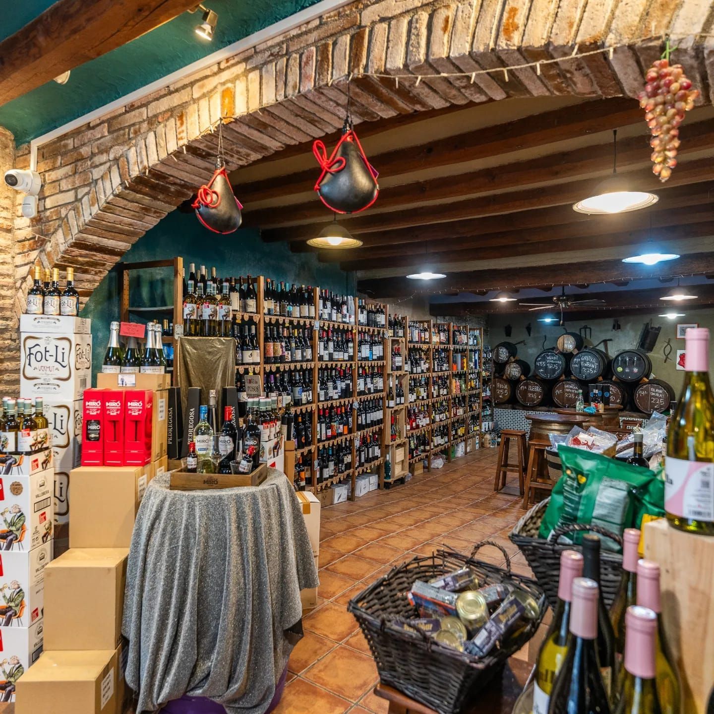 Una bodega rústica con estantes repletos de botellas, barriles de madera y una mesa de exposición cubierta con un paño.