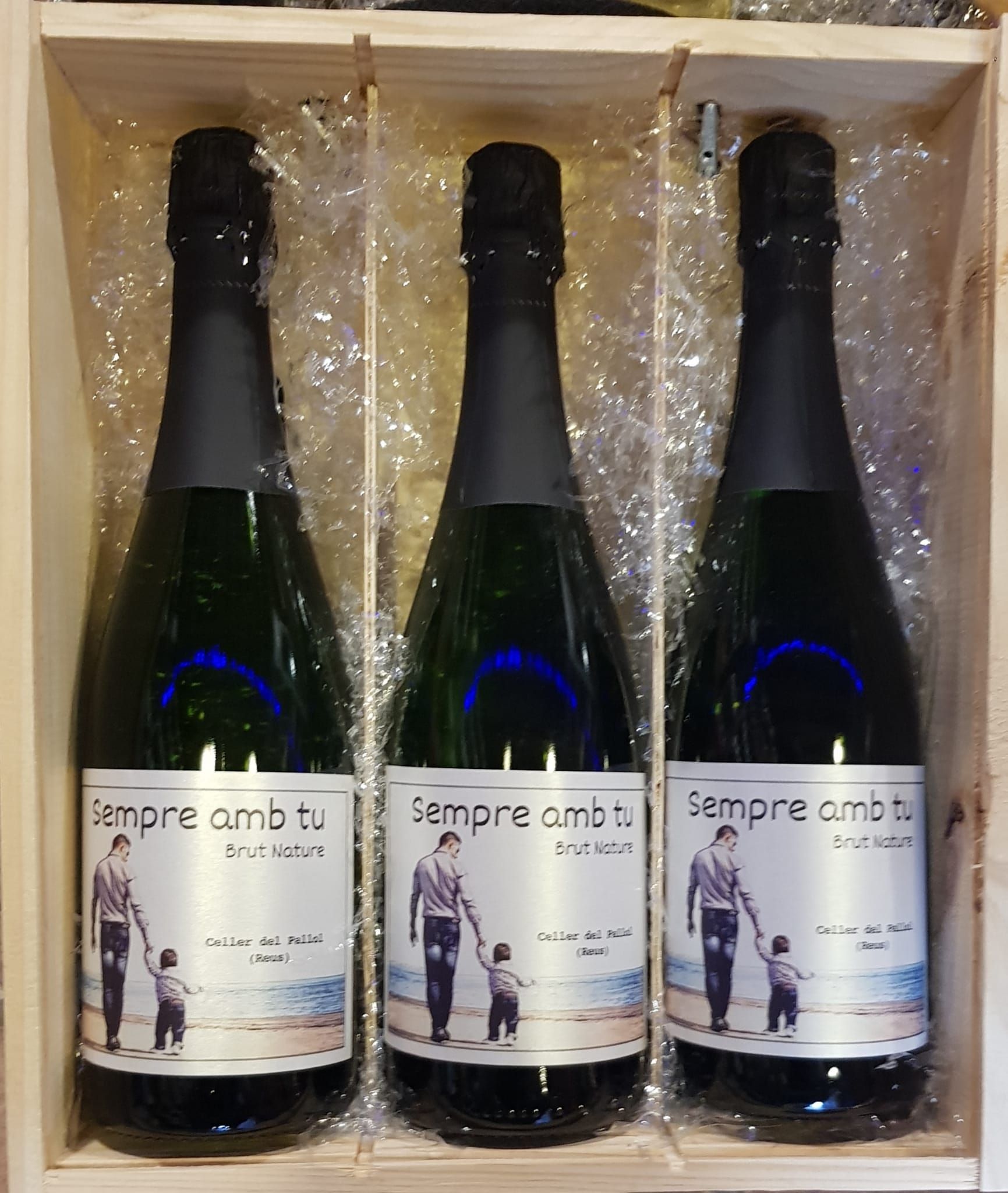 Tres botellas de vino espumoso en una caja de regalo de madera, cada una con una etiqueta personalizada 