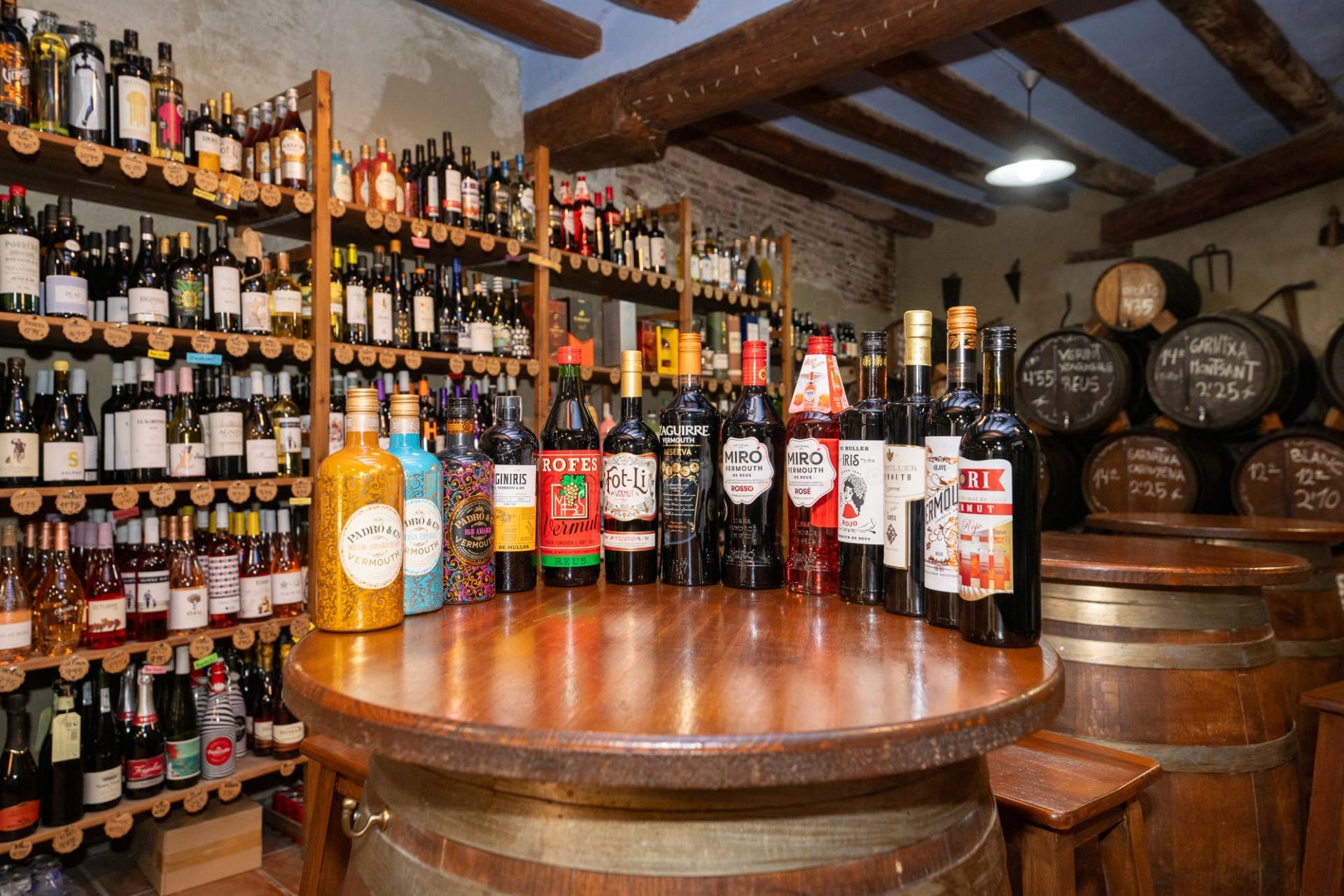 Una bodega rústica con numerosas botellas en estantes de madera y una mesa central hecha con un barril.