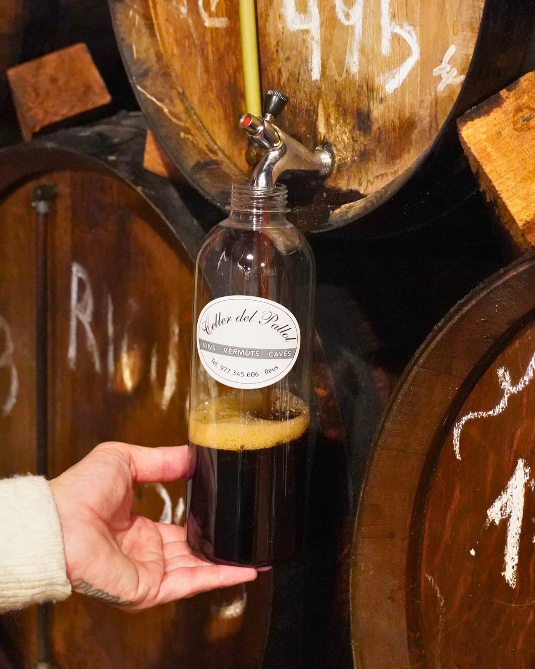 Una mano sostiene una botella de plástico que se está llenando con vino tinto oscuro procedente 