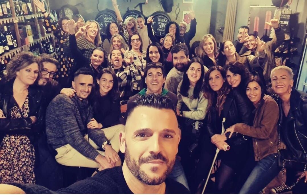 Un numeroso grupo de personas sonríe para hacerse un selfie dentro de un bar con poca luz