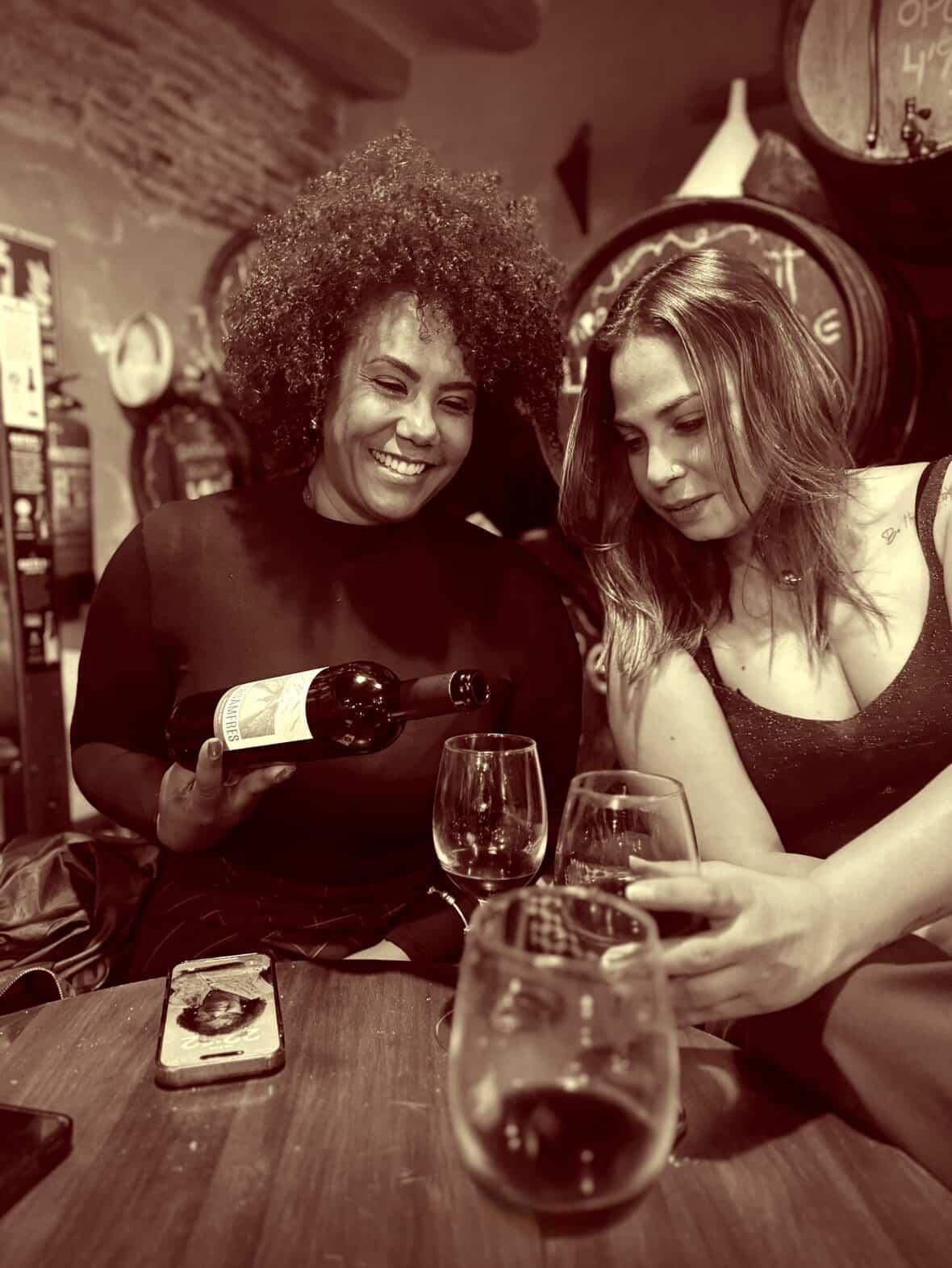 Dos personas están sentadas a una mesa de madera en una bodega rústica y con poca luz, sonriendo mientras