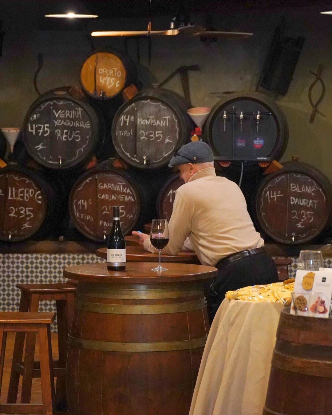 Un individuo con una camisa color canela está sentado en una mesa hecha con un barril de vino