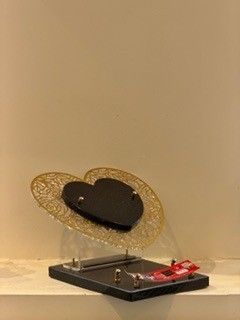 Un cœur en filigrane d'or avec un centre noir sur une base noire, un petit objet rouge à la base.