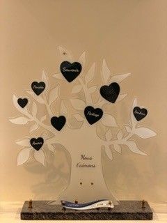 Arbre commémoratif orné de plaques nominatives noires en forme de cœur, reposant sur un socle en pierre.