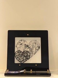 Plaque funéraire avec un tableau encadré de noir avec deux cœurs ; un dessin floral et un motif découpé.