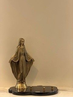 Statue de la Vierge Marie aux bras ouverts, teinte bronze, sur socle noir.