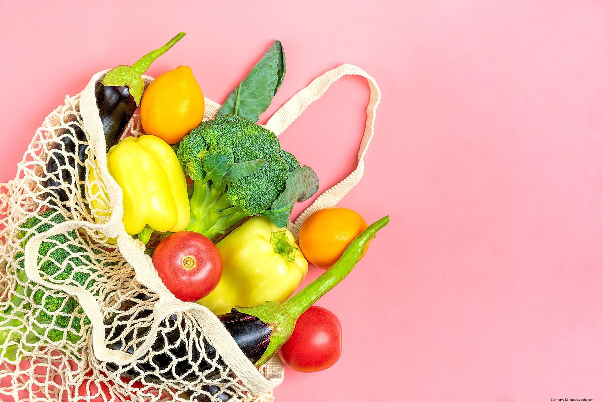 Ein Netzbeutel mit frischem Obst und Gemüse auf rosafarbenem Hintergrund