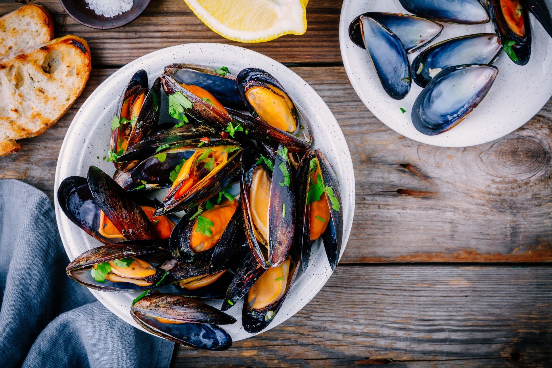 Des bols de moules cuites avec des quartiers de citron sur une table rustique en bois.