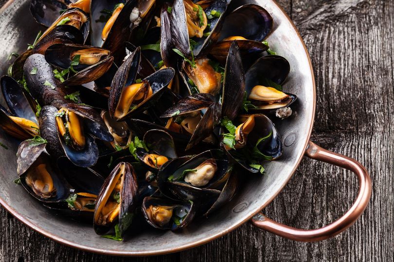 Poêlée de moules cuites sur une table rustique en bois.