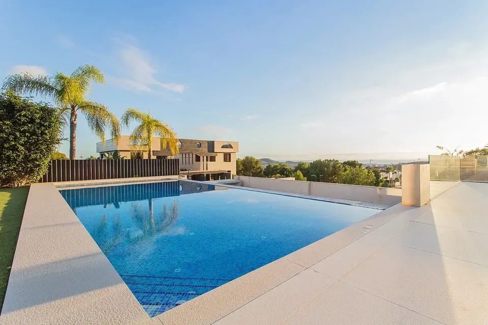 Piscina privada rodeada de zonas verdas bajo un cielo azul despejado. 