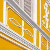 Sonnengelbe Hausfassade mit weiß gestrichenen Wandverzierungen