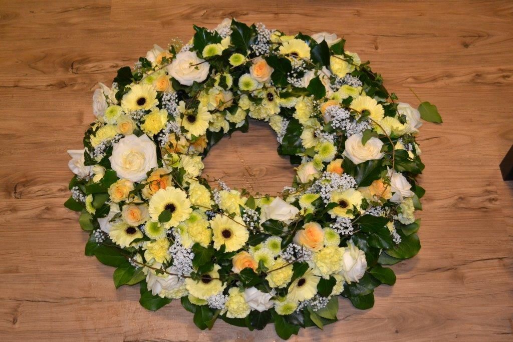 Auf einem Holzboden liegt ein Kranz aus gelben und weißen Blumen.