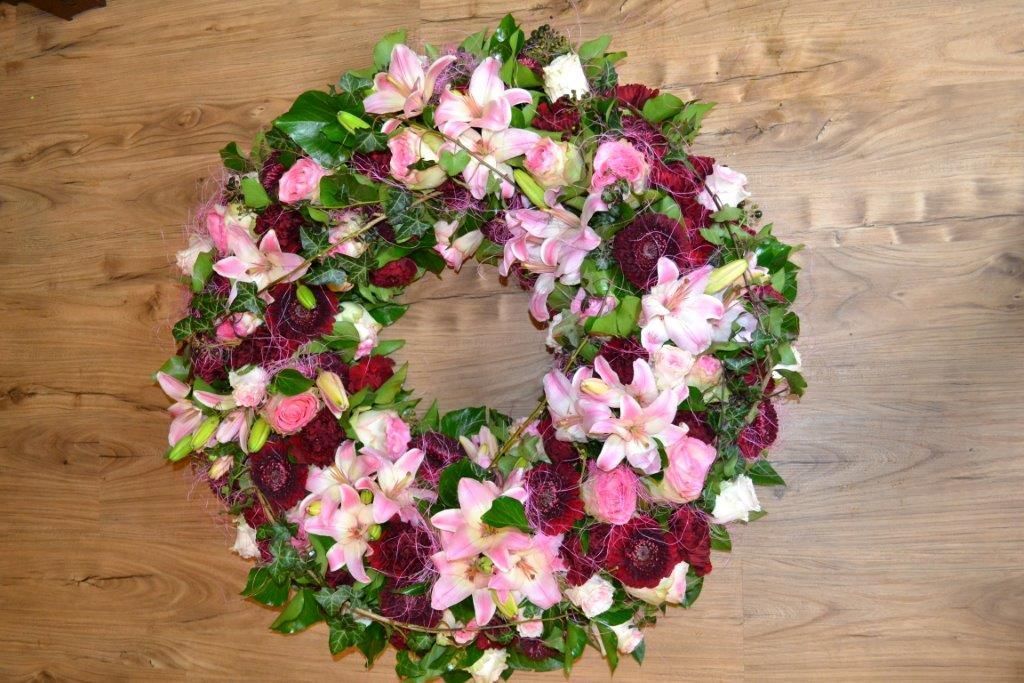 Auf einem Holztisch steht ein Kranz aus rosa und violetten Blumen.