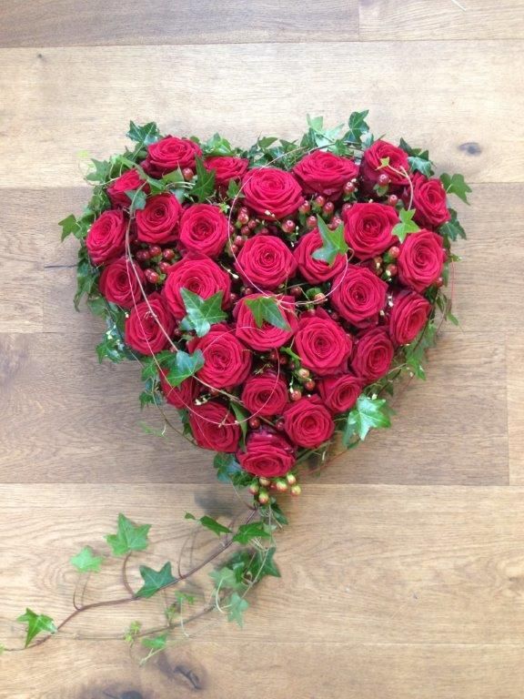 Ein herzförmiges Arrangement aus roten Rosen und Efeu auf einem Holztisch.