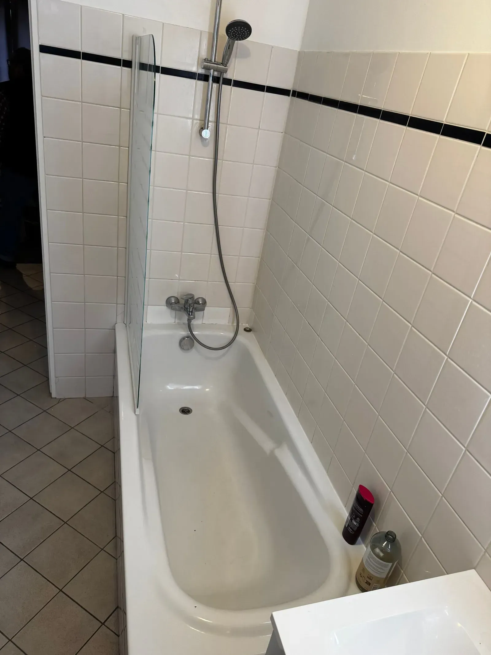 Baignoire blanche avec pommeau de douche, à côté de murs carrelés et d'un rideau de douche.