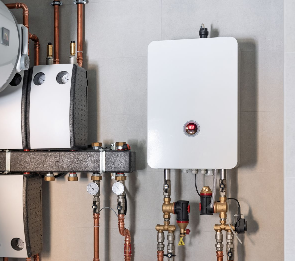 Chaudière électrique et tuyaux associés montés sur un mur gris clair dans un environnement intérieur.