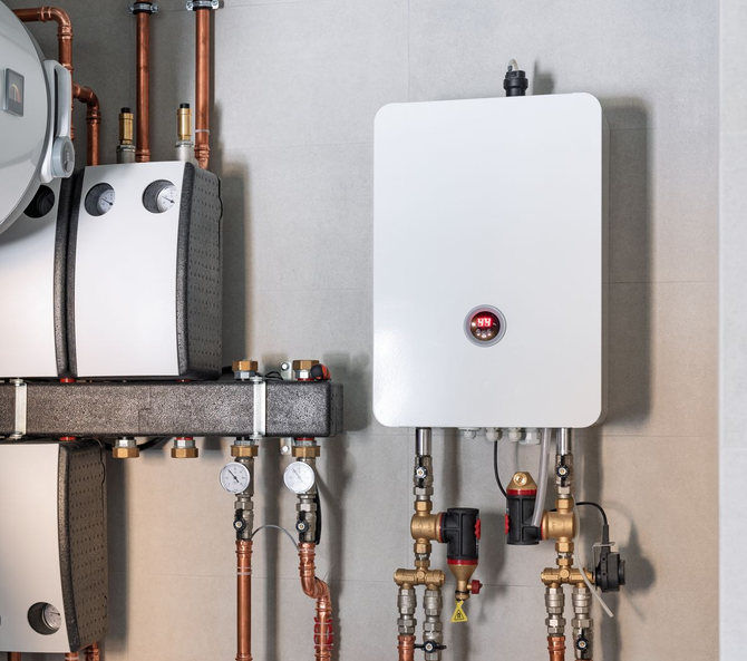 Chaudière électrique et tuyaux associés montés sur un mur gris clair dans un environnement intérieur.