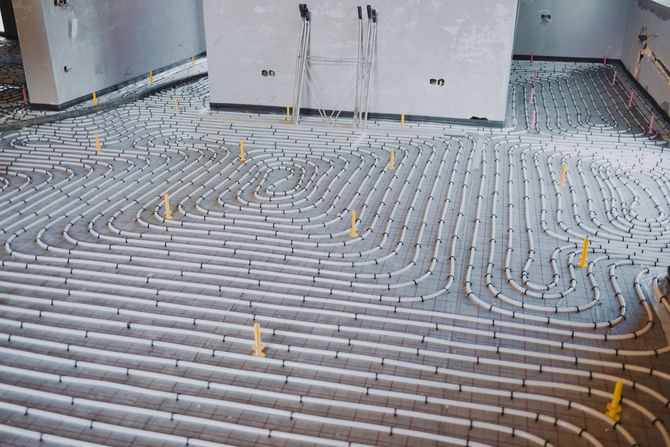 Tuyaux posés sur un sol en béton, formant un système de chauffage. Chantier de construction, principalement gris et blanc.