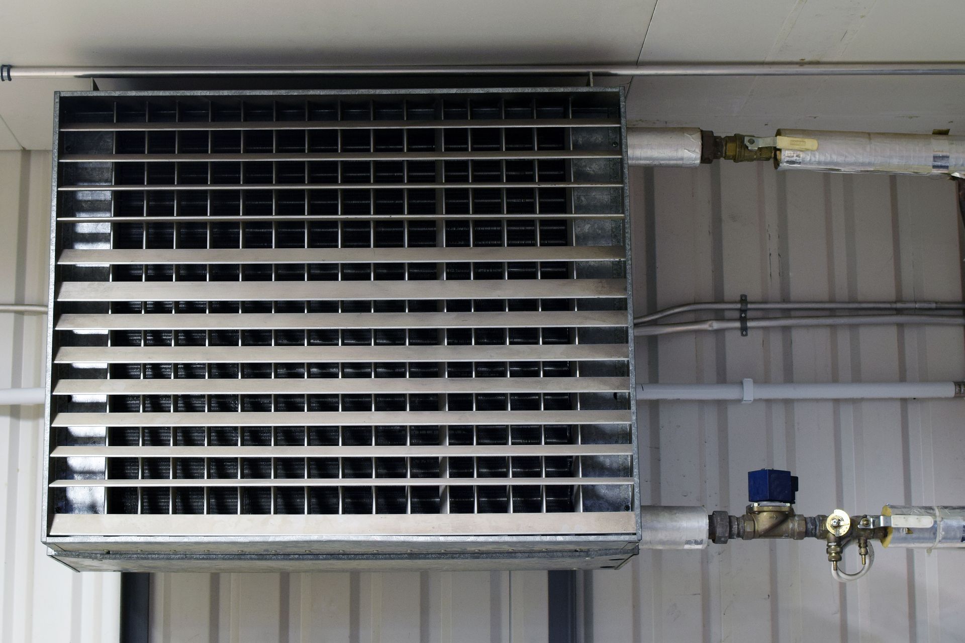 Chauffage mural en métal monté sur un mur blanc avec conduites de gaz attachées.