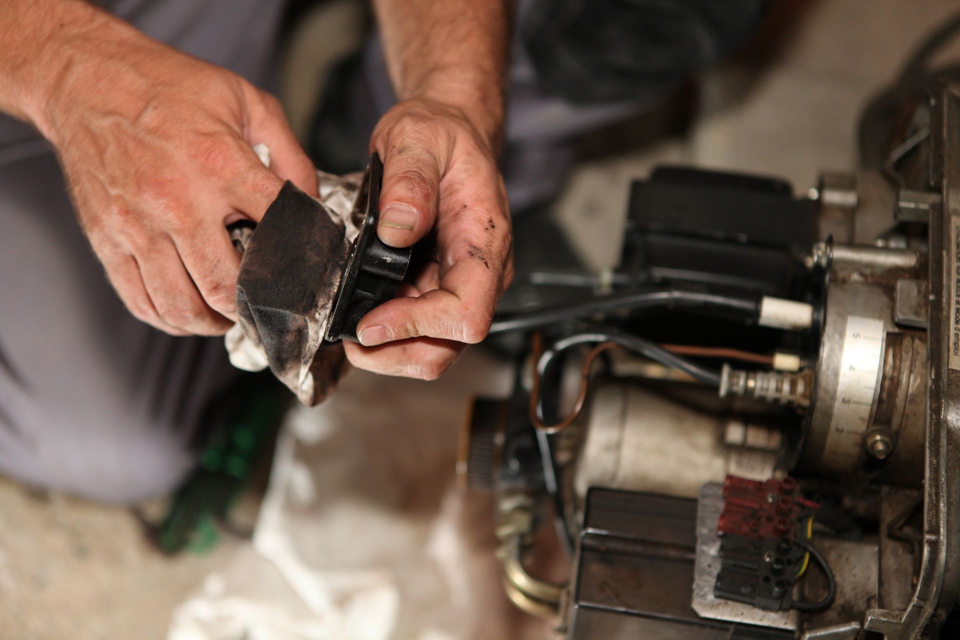 Mains tenant une pièce noire et sale au-dessus d'un brûleur de chaudière à fioul.