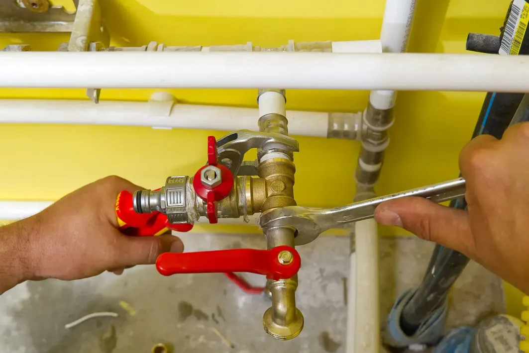 Plombier utilisant une clé pour serrer une vanne sur une conduite d'eau. Fond jaune. Robinetterie rouge et argent.