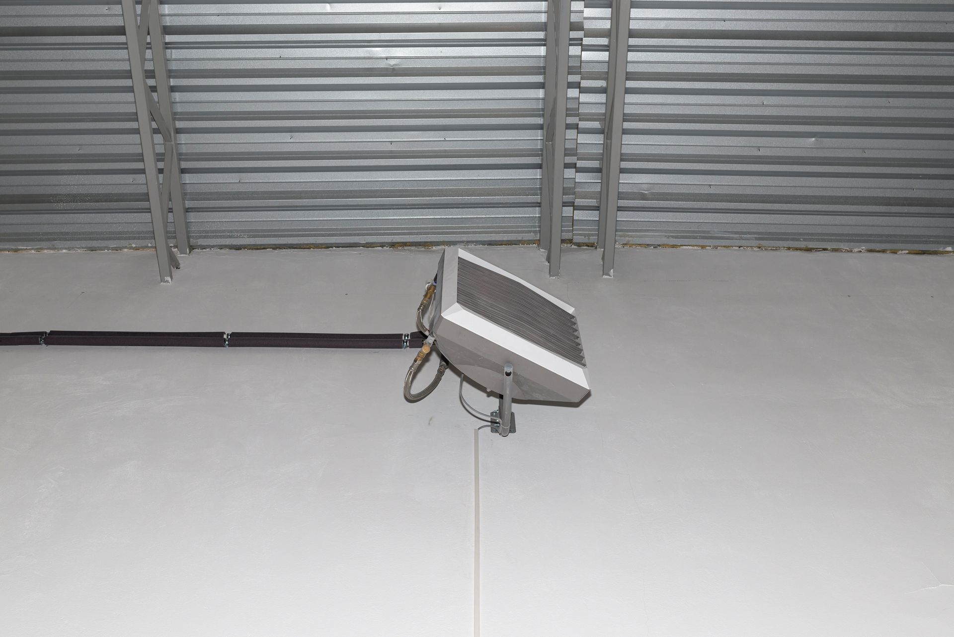 Aérotherme fixé à un mur blanc sous un plafond en métal ondulé.