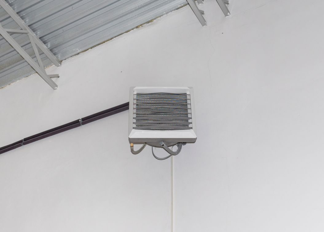 Une unité de chauffage industrielle est montée sur un mur blanc sous un plafond métallique.