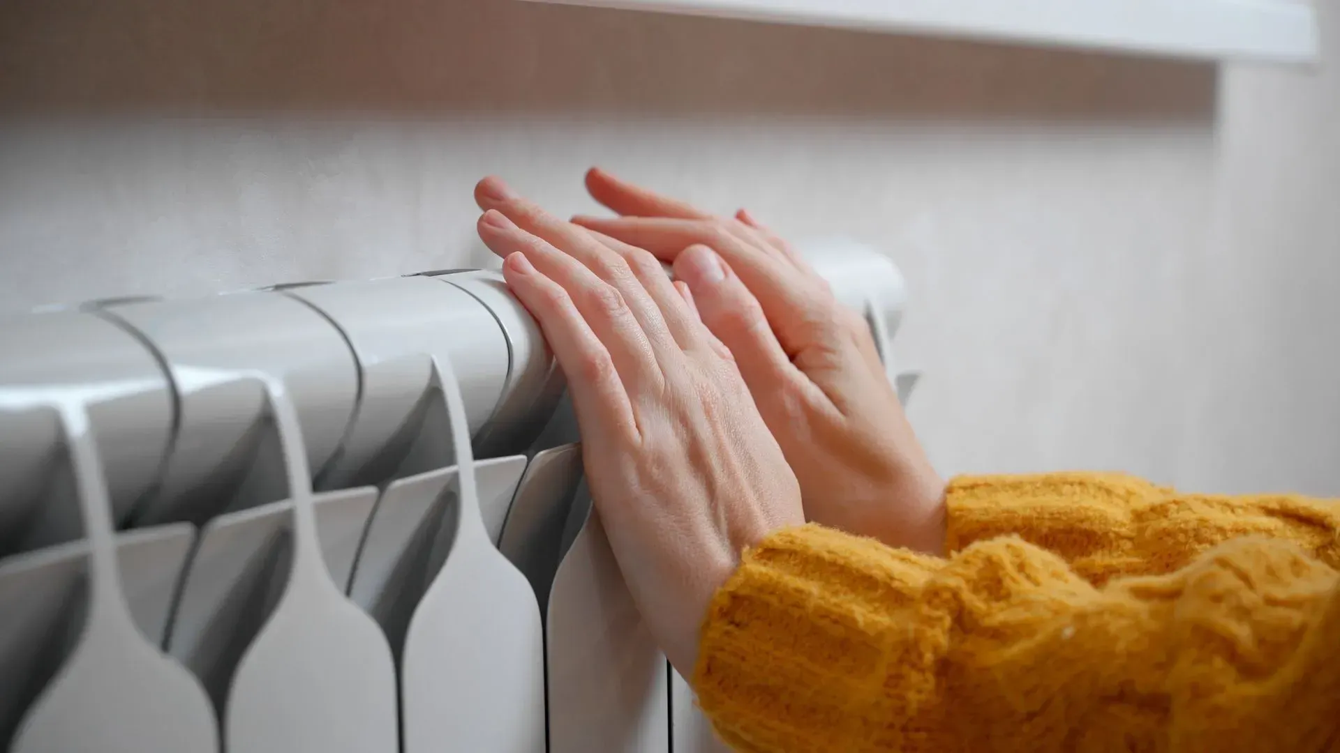 Mains se réchauffant sur un radiateur blanc ; personne portant un pull jaune.