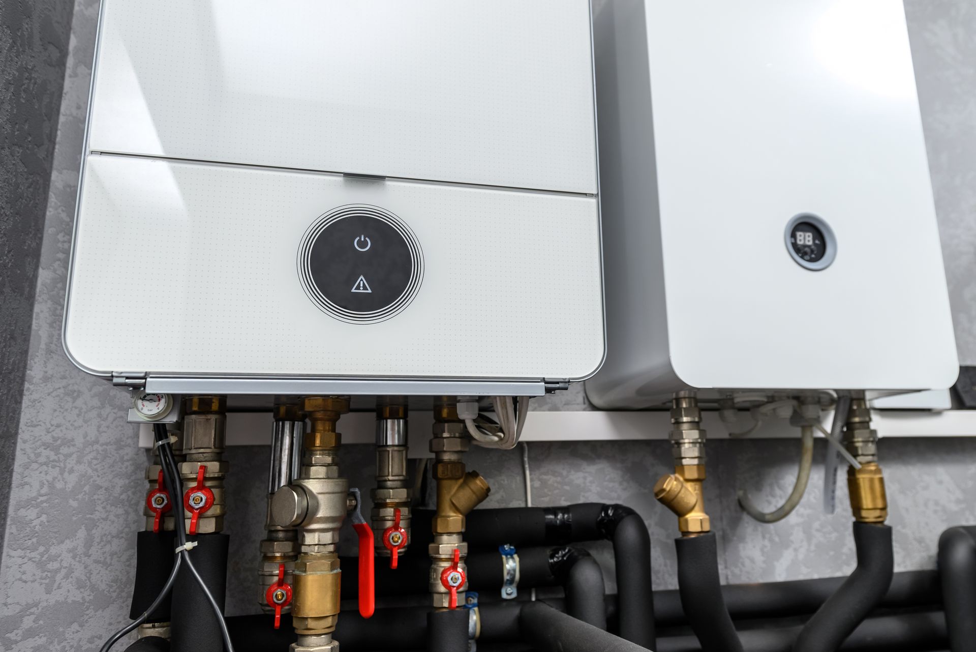 Deux chaudières électriques montées sur un mur avec divers tuyaux et vannes.