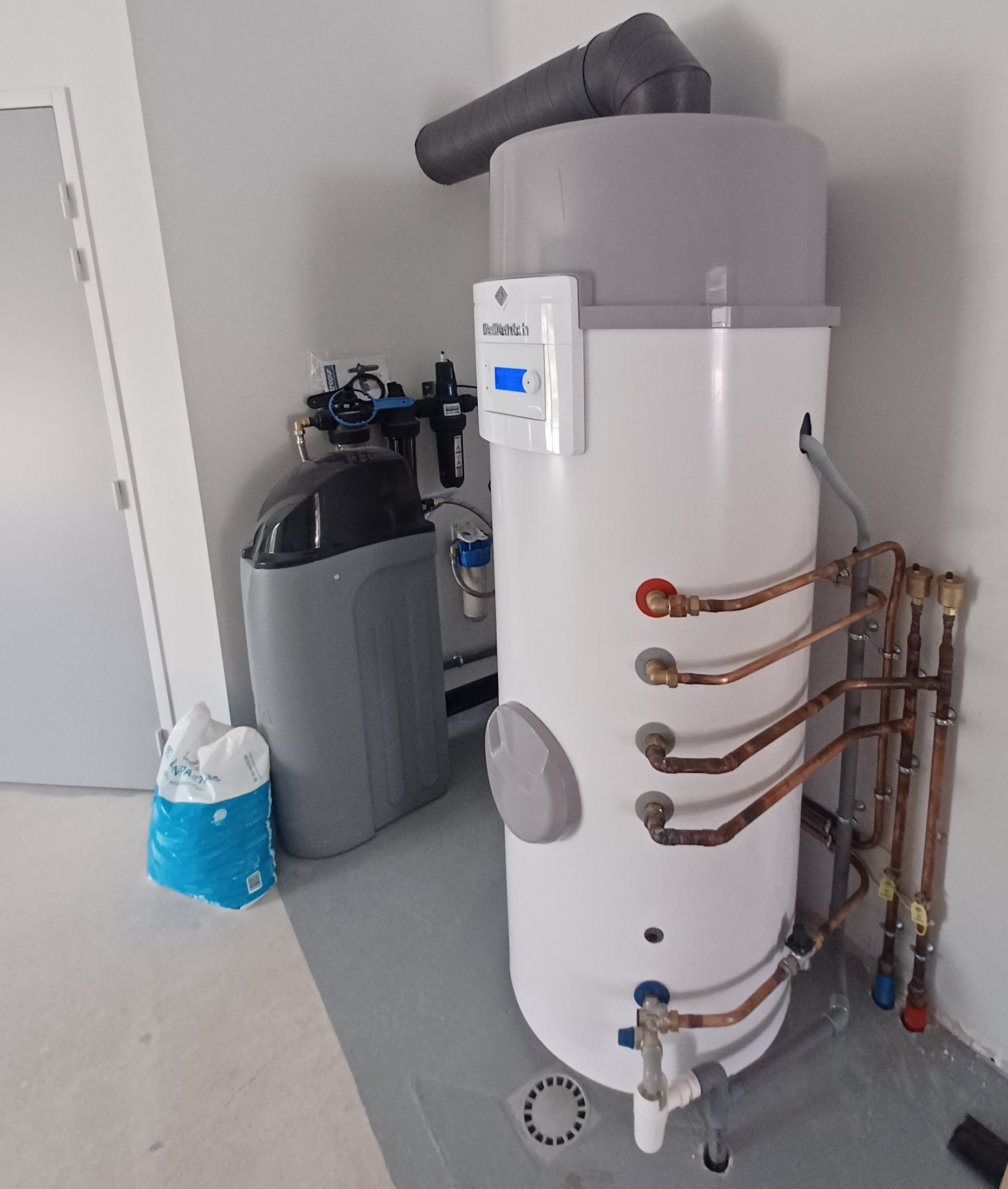 Plombier utilisant une clé sur un raccordement de chauffe-eau dans une maison.