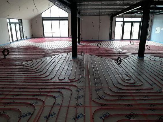 Tubes chauffants radiants rouges installés sur un plancher en béton dans un bâtiment.