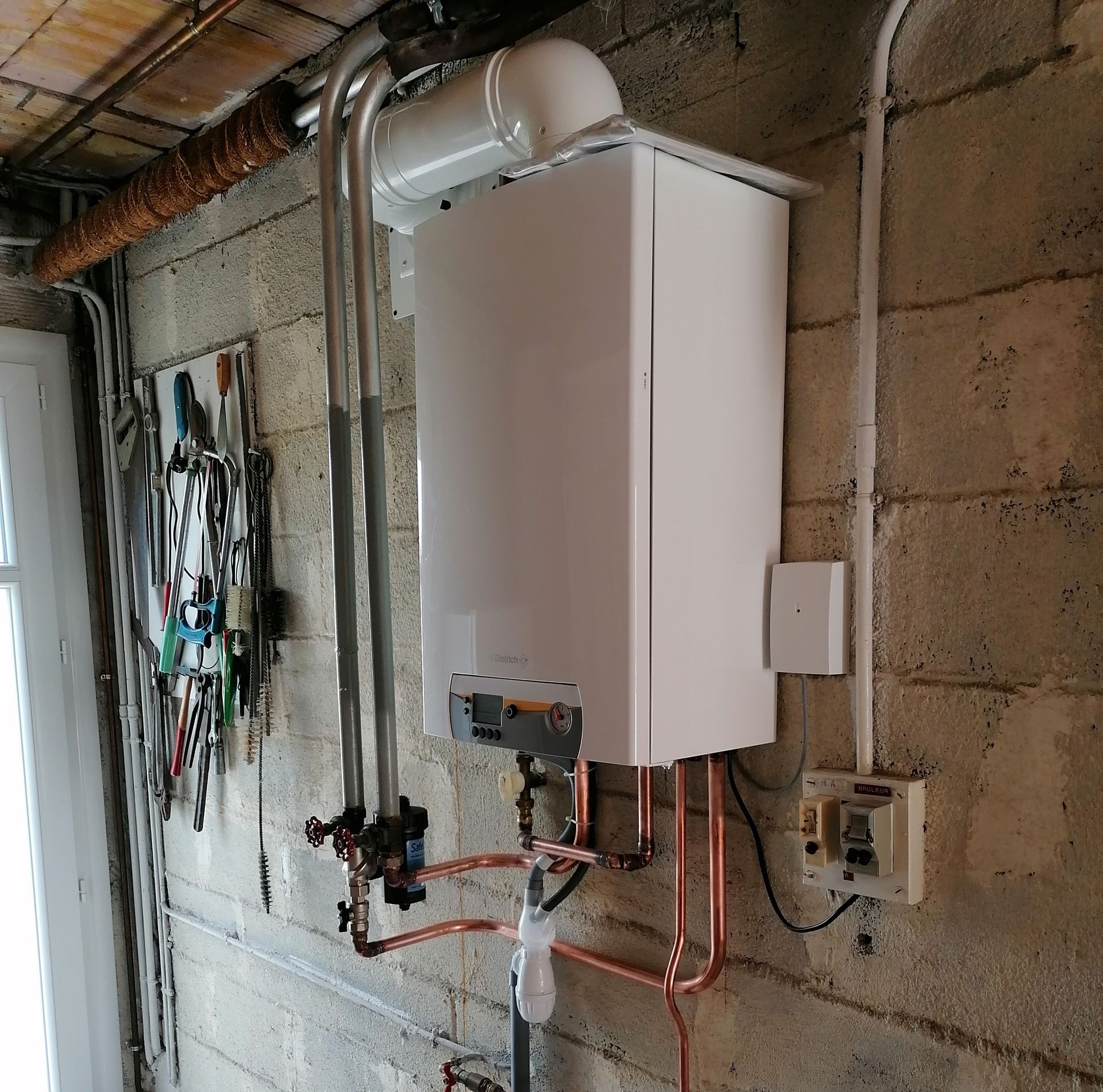 Chaudière à gaz murale blanche avec conduit et tuyaux de gaz jaunes.