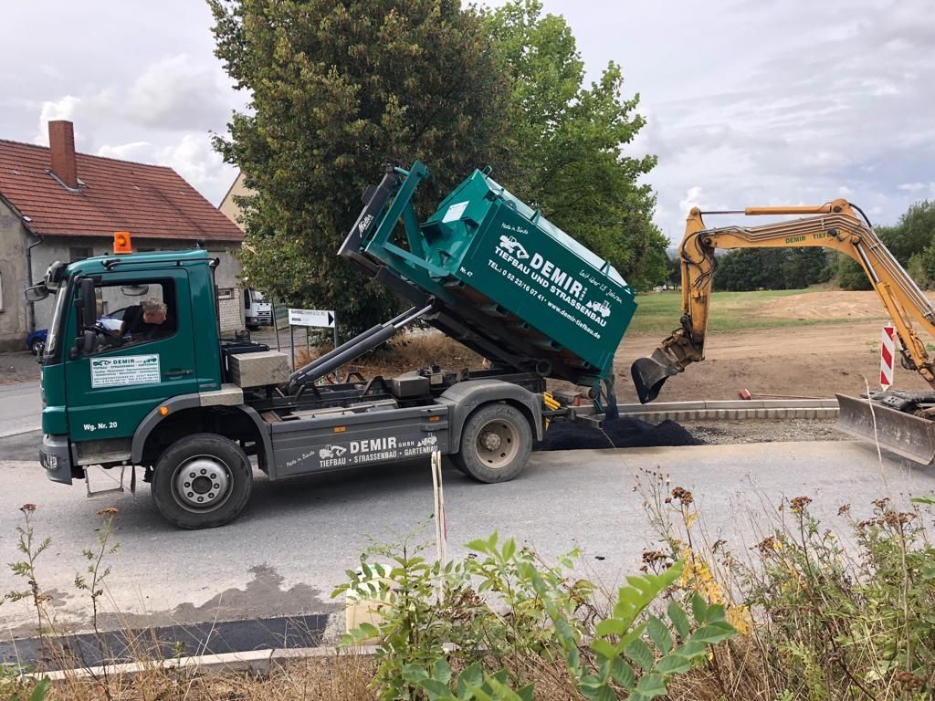 Ein grüner Muldenkipper fährt neben einem gelben Bagger auf einer Straße.