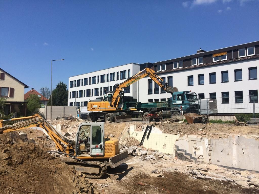 Eine Gruppe von Baufahrzeugen arbeitet auf einer Baustelle vor einem Gebäude.