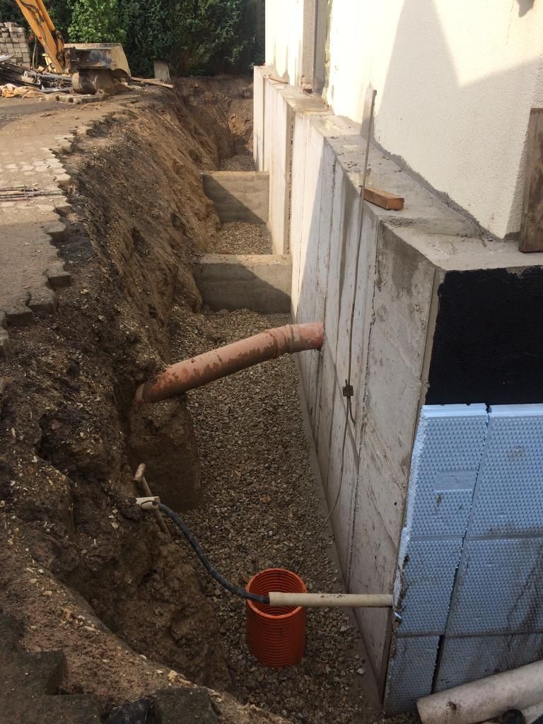 Aus einem Loch im Boden neben einem Gebäude kommt ein Rohr.