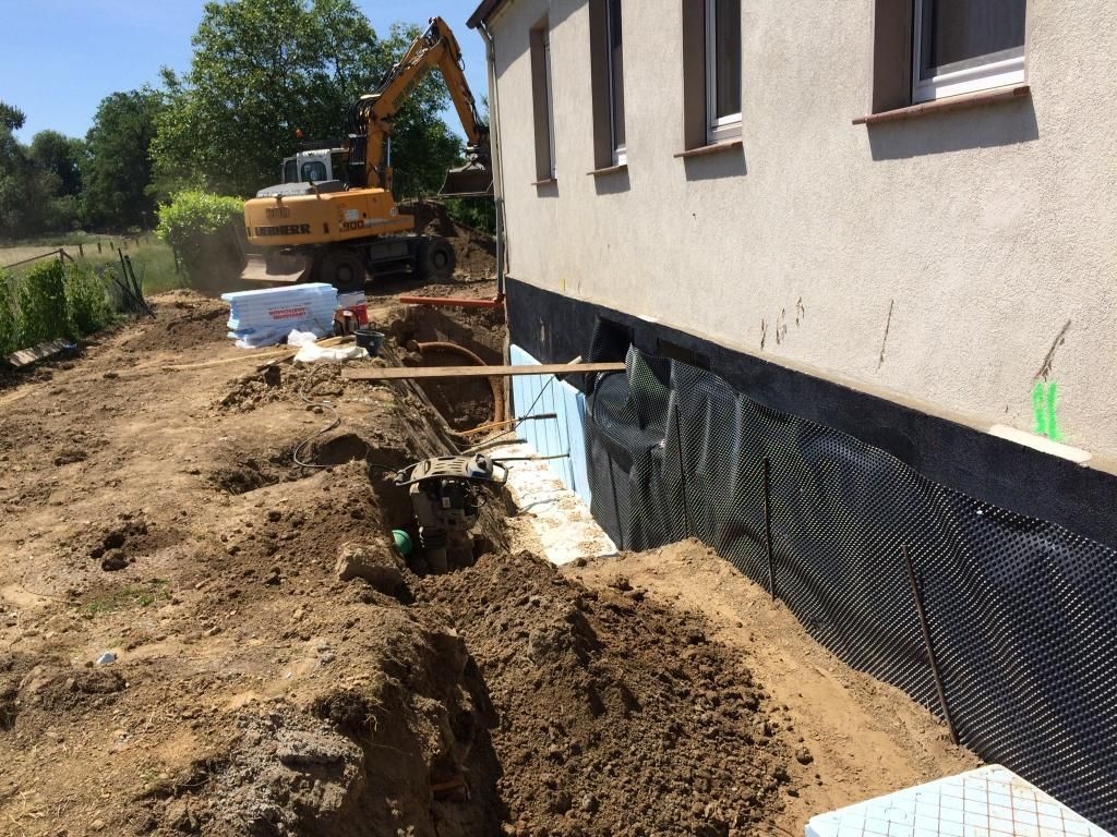 Ein großer gelber Bagger gräbt vor einem Haus ein Loch.