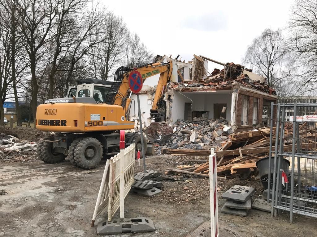 Ein großer gelber Bagger zerstört auf einer Baustelle ein Gebäude.