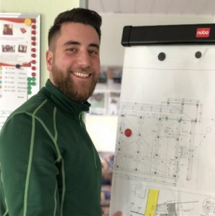 Ein Mann in einem grünen Hemd hält eine weiße Tafel mit einer Zeichnung darauf.