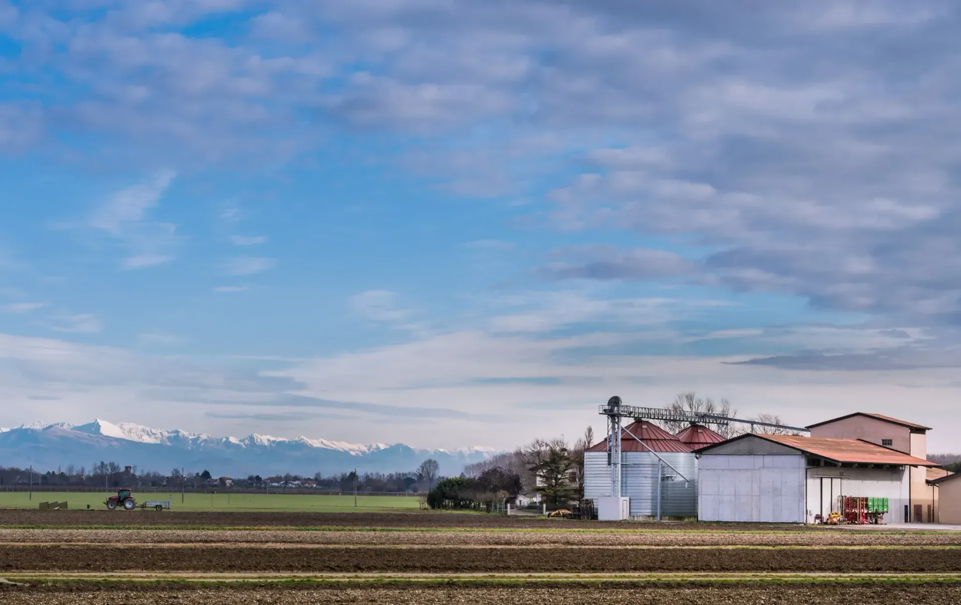 Edificios agrícolas en un campo bajo un cielo nublado, montañas en la distancia.
