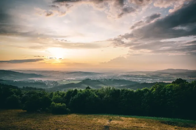 Puesta de sol sobre un bosque, con nubes en un cielo amarillo y naranja, y niebla en la distancia.