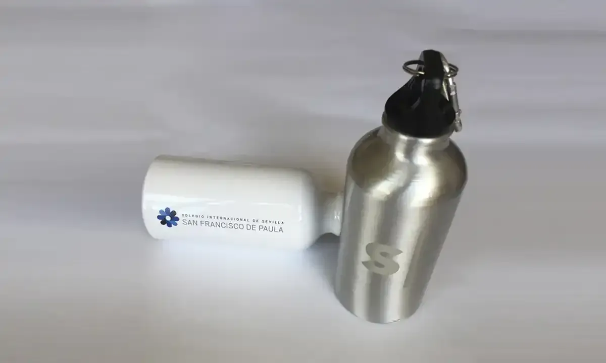 Botella de agua de acero inoxidable y tubo blanco, ambos con superficie blanca. La botella tiene un tapón negro y una 