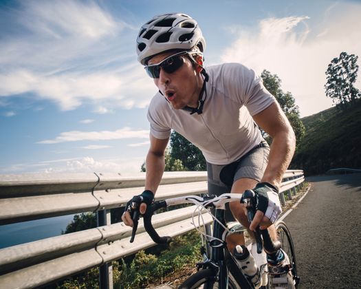 Un hombre que lleva casco y gafas de sol va en bicicleta por una carretera.