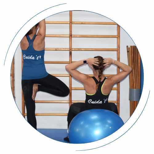 Una mujer está sentada sobre una pelota de ejercicio azul mientras otra mujer está haciendo yoga.