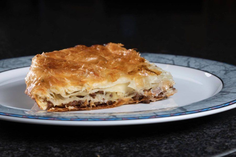 Ein Stück Burek liegt auf einem Teller auf einem Tisch. Foto von der Burek House GmbH.