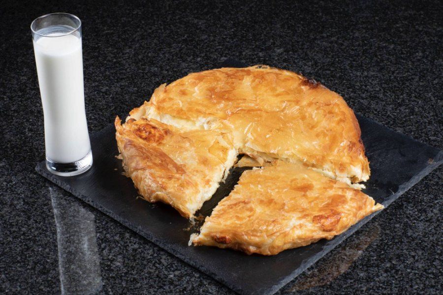 Ein Burek, aus dem ein Stück herausgeschnitten wurde, neben einem Glas Milch. Foto von der Burek House GmbH.